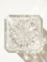 Load image into Gallery viewer, Clear glass block with a square shape and a circular faceted starburst pattern on top, photographed from above on a white background with soft shadows and light reflections.
