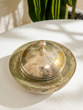 Load image into Gallery viewer, A vintage tarnished silver lidded ceramic or glass jar with a matching lid, resting on a white textured fabric surface with soft shadows and a plant in the background.

