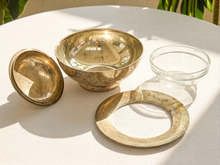 Load image into Gallery viewer, A brass-toned metal bowl set with a matching lid and a clear glass bowl, arranged on a white tablecloth in natural sunlight.
