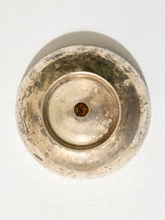 Load image into Gallery viewer, A top-down view of a round, vintage tarnished metal bowl or dish with a small central hole, resting on a textured off-white fabric background.
