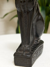 Load image into Gallery viewer, Close-up of a dark brown carved Egyptian cat statue on a white surface with a blurred green plant in the background.
