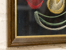 Load image into Gallery viewer, Close-up of a framed wall art piece showing colorful string embroidery on a black background, with a dark wood frame and gold inner trim mounted on a white textured wall.
