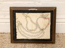 Load image into Gallery viewer, A framed vintage quilt pattern book or instruction sheet with a wooden frame, displayed on a woven rug against a white painted wood wall.
