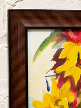 Load image into Gallery viewer, A close-up of a framed abstract floral painting, showing a dark brown wood frame against a white textured wall. The artwork features bold yellow, green, red, and blue brushstrokes on a cream background.
