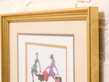 Load image into Gallery viewer, A close-up of a gold-framed art print with a beige mat, showing a partial fashion illustration of two women walking on a white background, mounted against a textured off-white brick wall.
