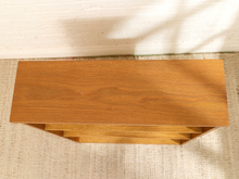 Load image into Gallery viewer, A mid-century modern wooden console table with a warm oak finish, photographed from a top-down angle against a white brick wall and textured beige rug.

