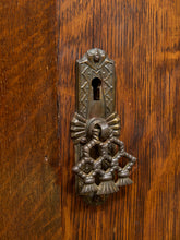 Load image into Gallery viewer, An ornate antique-style metal keyhole cover and keyrue set on a warm brown wooden door.
