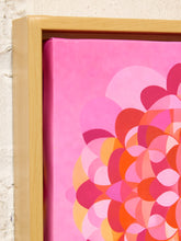 Load image into Gallery viewer, A close-up of a framed canvas wall art print featuring a bold, retro-style floral or circular pattern in shades of pink, magenta, orange, and yellow, set in a light natural wood frame against a textured off-white wall.

