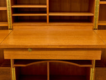 Load image into Gallery viewer, Close-up of a wooden writing desk with a pull-out desktop, a drawer front, brass corner brackets, and open shelving behind it.
