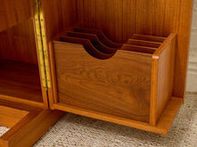 Load image into Gallery viewer, A close-up of a wooden storage organizer or drawer with multiple curved compartments, shown inside a larger wooden cabinet. The product is made of warm medium-brown wood with visible grain, and part of a brass hinge and woven rug are visible in the background.
