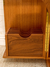 Load image into Gallery viewer, Close-up of a warm medium-brown wooden cabinet interior with a curved drawer or organizer compartment, brass hinge hardware, and a light woven rug visible at the bottom.
