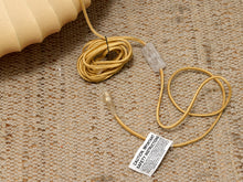Load image into Gallery viewer, A coiled gold-colored electrical cord with clear plastic connectors and a white warning label, laid on a textured beige woven mat next to a beige foam object.
