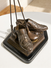 Load image into Gallery viewer, A bronze sculpture of a pair of loafers and golf clubs mounted on a black square base, displayed on a white surface with a softly blurred indoor background.
