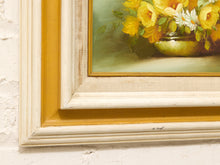 Load image into Gallery viewer, Close-up of a framed still life painting showing yellow flowers in a green bowl, with a distressed cream and yellow frame against a white textured wall.
