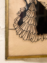 Load image into Gallery viewer, A close-up of a framed wall art piece showing a stylized black-and-beige ruffled dress silhouette on a warm beige background, with a gold-toned frame against a white wall.

