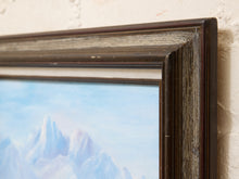 Load image into Gallery viewer, Close-up of a framed landscape painting showing snowy mountain peaks under a pale blue sky, with a dark rustic wooden frame against a textured off-white wall.
