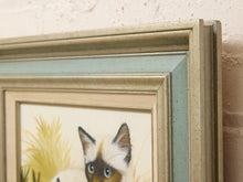 Load image into Gallery viewer, A close-up of a framed art print featuring a kitten illustration, showing a distressed light blue-green inner frame layered over a wider beige frame against a textured cream wall.
