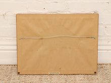 Load image into Gallery viewer, The back of a square tan canvas or wood-mounted art piece, showing a thin wire stretched horizontally across the center and two small metal loops at the bottom corners, photographed against a white painted brick wall and woven rug.
