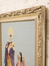 Load image into Gallery viewer, A close-up of an ornate vintage-style gold frame holding a needlepoint or embroidered artwork depicting two figures against a pale blue-gray background.
