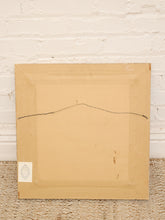 Load image into Gallery viewer, The back of a square framed artwork or print, showing a tan paper backing, a thin hanging wire or string across the center, and a small white label in the lower left corner, set against a white brick wall and woven rug.

