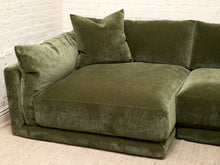 Load image into Gallery viewer, An olive green velvet sectional sofa with matching throw pillows, set against a white brick wall and light beige carpet.
