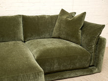 Load image into Gallery viewer, An olive green velvet sectional sofa with matching throw pillows, set against a white brick wall background.
