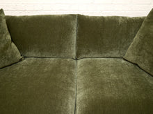 Load image into Gallery viewer, An olive green velvet loveseat sofa with matching throw pillows, set against a white brick wall background.
