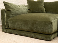 Load image into Gallery viewer, An olive green velvet sofa with matching throw pillows, positioned against a white brick wall on a light beige carpet.
