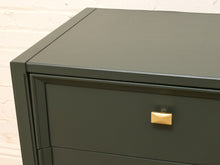 Load image into Gallery viewer, Close-up of a dark green metal filing cabinet with a gold rectangular pull handle, set against a white brick wall background.
