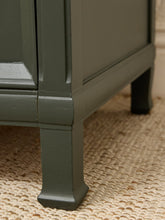 Load image into Gallery viewer, Close-up of a painted wooden cabinet leg in a muted sage green, standing on a woven beige rug.
