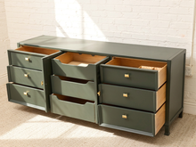 Load image into Gallery viewer, A dark green 8-drawer dresser with multiple drawers pulled open to show the light wood interiors, set against a white brick wall and beige carpet.

