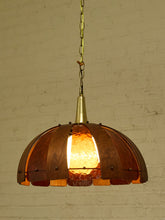 Load image into Gallery viewer, A vintage-style pendant light with a dome-shaped shade made of warm copper-toned metal and amber glass panes, hanging against a white brick wall.

