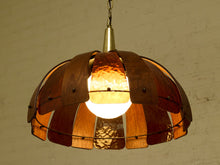 Load image into Gallery viewer, A rustic hanging pendant light with a dome-shaped shade made of overlapping copper-toned metal plates and a glowing white globe bulb, set against a textured off-white wall.
