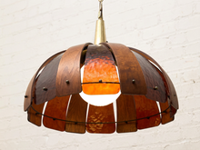 Load image into Gallery viewer, A mid-century modern pendant light with a dome-shaped shade made of layered dark brown wood and amber-orange stained glass panels, suspended against a white brick wall.
