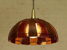 Load image into Gallery viewer, A vintage-style pendant light with a dome-shaped shade made of overlapping amber-tinted glass and dark wood slats, hanging against a white brick wall.
