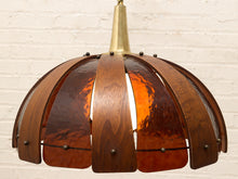 Load image into Gallery viewer, A mid-century modern pendant light with a dome-shaped shade made of curved dark wood slats and amber glass panels, suspended from a brass rod against a white brick wall.
