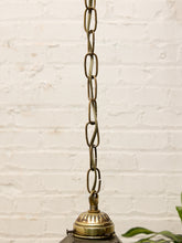 Load image into Gallery viewer, A close-up of a hanging brass pendant light fixture showing the chain, top cap, and part of the glass shade against a white brick wall background.
