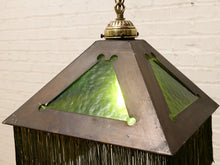 Load image into Gallery viewer, Close-up of a vintage-style pendant light fixture with a dark bronze metal frame, green textured glass panels, and a hanging fringe, shown against a white brick wall.
