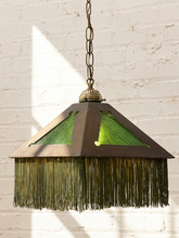 Load image into Gallery viewer, A vintage-style pendant light with a dark bronze metal frame, green glass panels, and a long fringe shade, hanging against a white brick wall.
