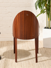 Load image into Gallery viewer, A mid-century modern wooden chair with a rounded, dome-shaped backrest and four tapered legs, made of rich reddish-brown wood with visible grain, set against a white brick wall and a beige woven rug.
