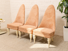 Load image into Gallery viewer, Three matching high-back accent chairs with textured peach-orange and cream patterned upholstery and turned cream legs, arranged against a white brick wall.
