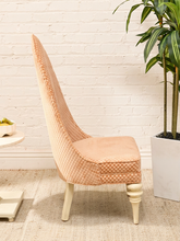 Load image into Gallery viewer, A high-back accent chair upholstered in a peach and cream checkered fabric, set against a white brick wall with a potted plant and a small side table nearby.
