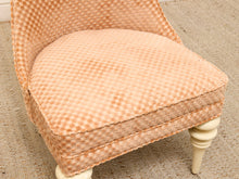 Load image into Gallery viewer, A close-up of an upholstered accent chair with a peach and beige checkered patterned fabric, cream-colored turned legs, and a curved backrest, set on a textured beige carpet.
