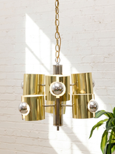 Load image into Gallery viewer, Vintage Space Age chandelier with polished brass cylindrical shades, mirrored chrome spheres, multiple lights, and chain suspension
