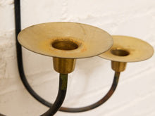 Load image into Gallery viewer, Close-up of a two-light brass wall sconce with a black metal frame, mounted against a white brick wall.
