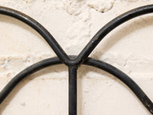 Load image into Gallery viewer, Close-up of a black metal bed frame rail crossing over a distressed off-white brick wall background.
