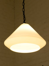 Load image into Gallery viewer, A warm white cone-shaped pendant light with a black hanging chain, shown against a dark textured brick wall background.

