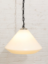 Load image into Gallery viewer, A hanging pendant light with a warm white frosted glass shade and a black metal chain, shown against a white painted brick wall.
