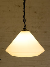 Load image into Gallery viewer, A hanging pendant light with a warm white frosted glass shade and a black chain, shown against a white brick wall.
