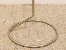 Load image into Gallery viewer, A close-up of a polished silver metal table base with a circular footrest and a vertical leg, resting on a textured beige woven rug.
